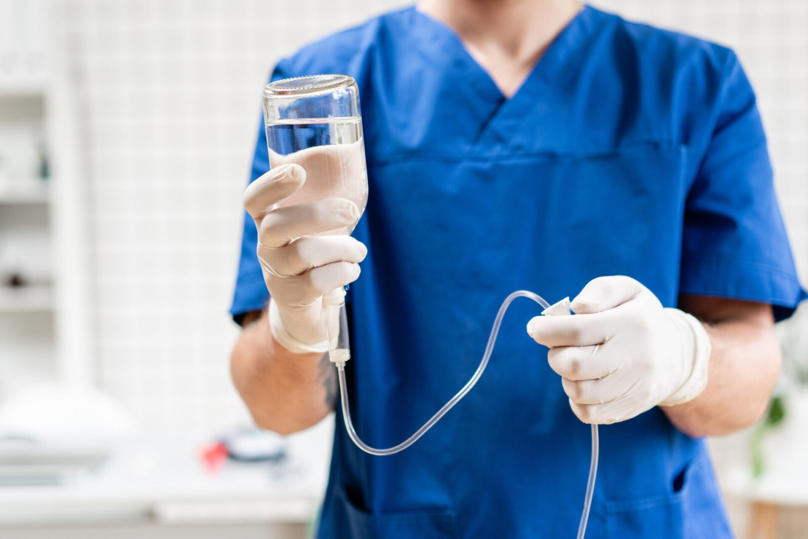 Healthcare professional in blue scrubs holds an IV bag and tube, preparing a medical procedure.