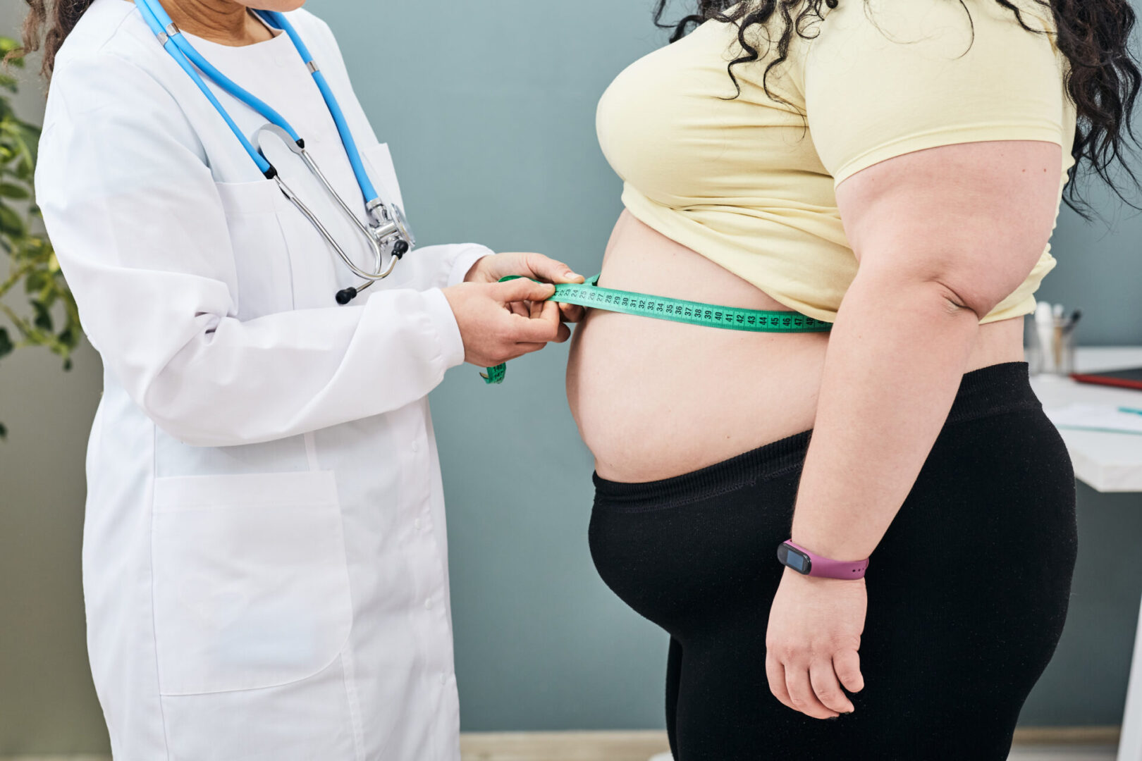 Obesity, unhealthy weight. Nutritionist inspecting a woman's waist using a meter tape to prescribe a weight loss diet